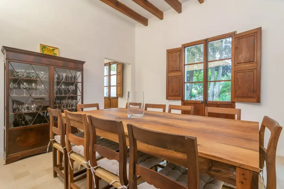 A dining room with a long wooden table and chairs beneath exposed ceiling beams.