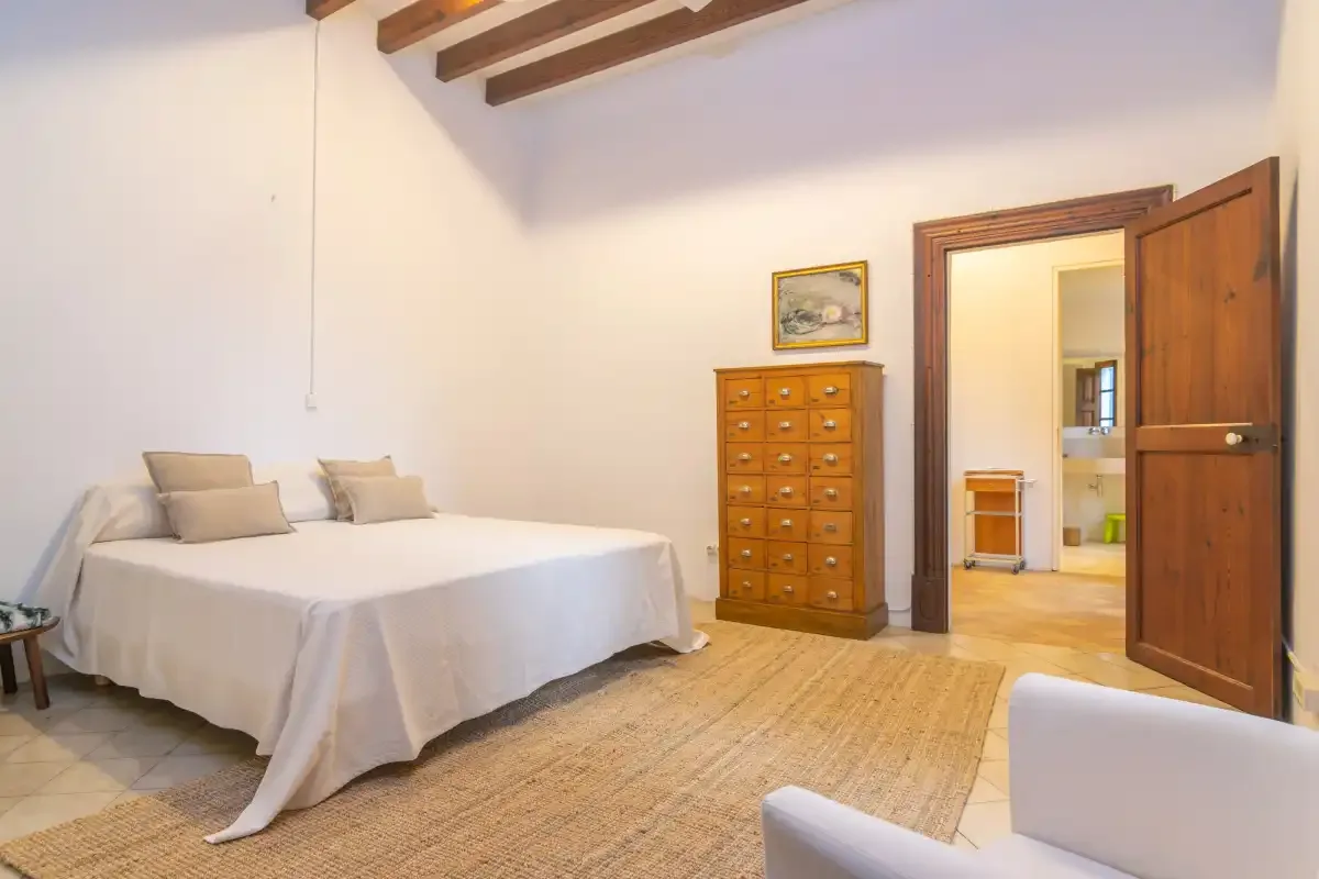 A bedroom with a bed, a wooden dresser, and an open doorway.
