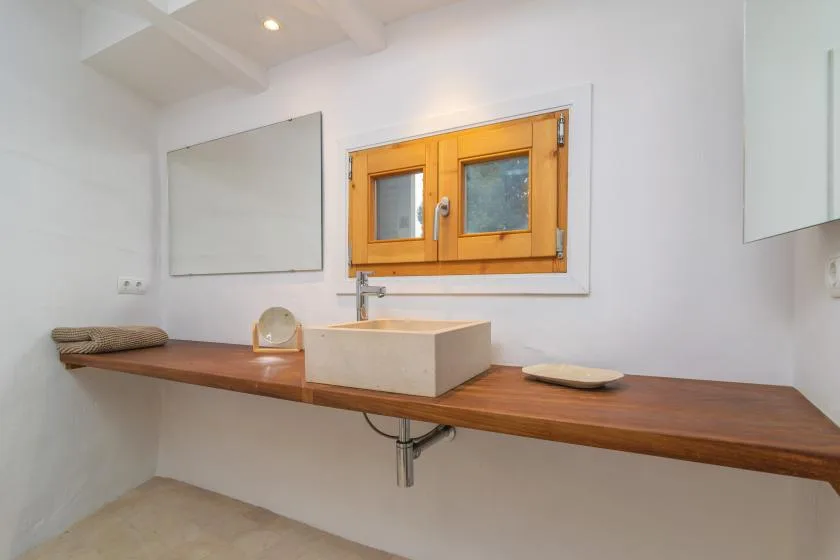 A bathroom vanity with a wooden counter, vessel sink, and small window.