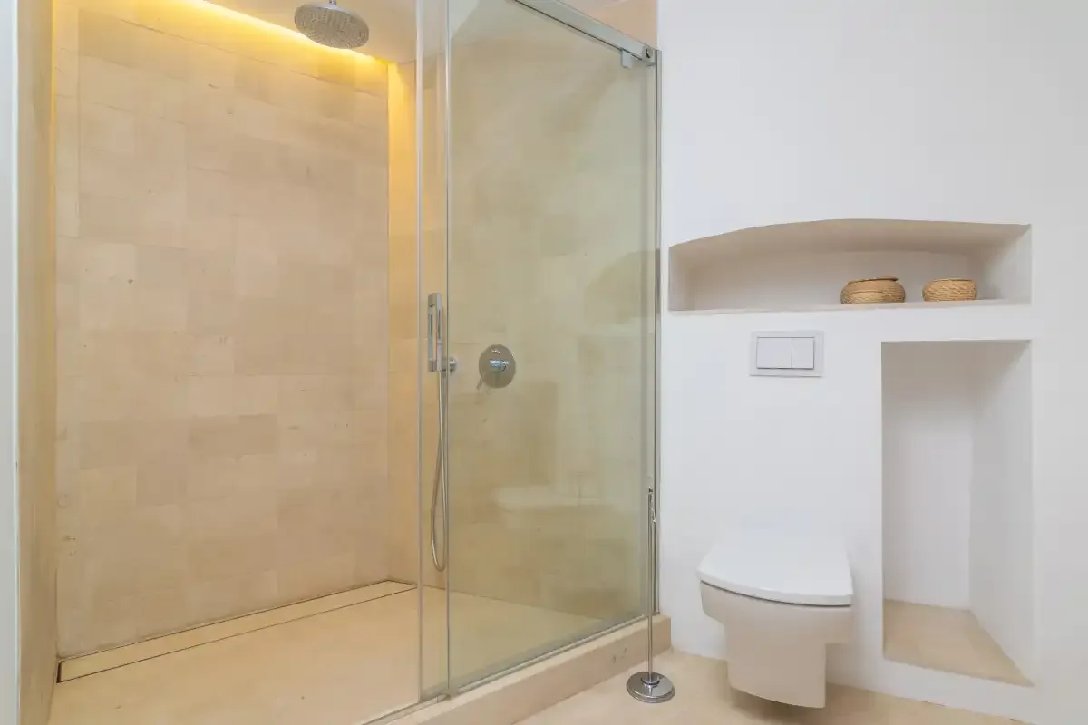 A bathroom with a glass shower and a toilet beside recessed wall shelves.