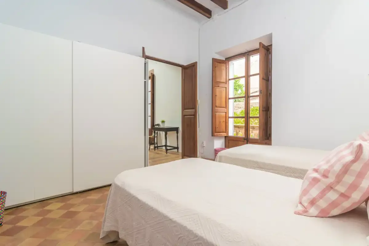 A bright bedroom with two beds and an open wooden window.