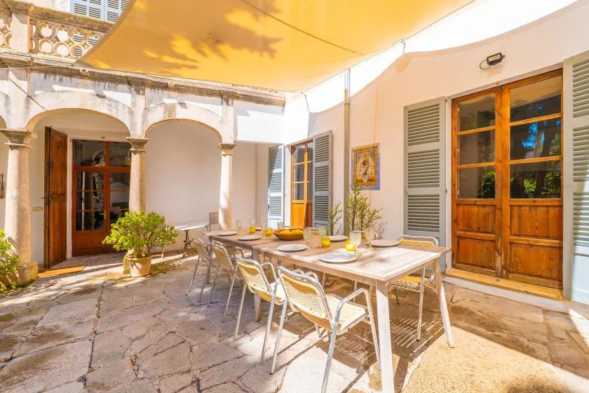 A shaded outdoor dining area with a long table and chairs beside wooden doors.