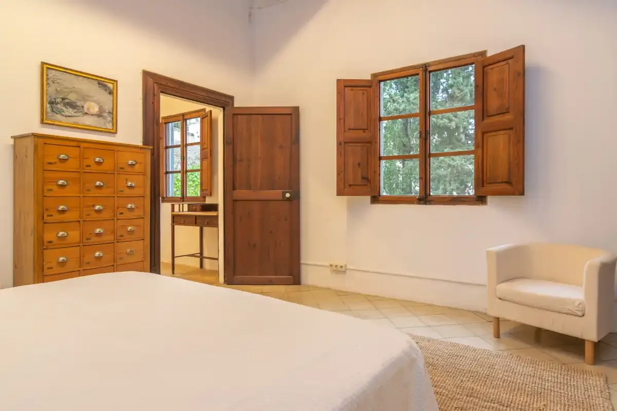 A bedroom with a bed, wooden furniture, and a window with open shutters.