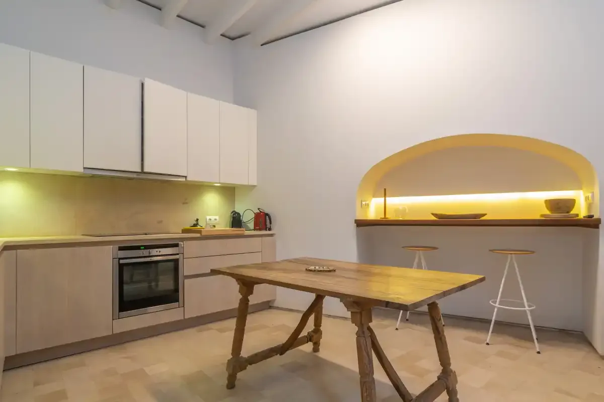 A kitchen and dining area with a wooden table and illuminated serving counter.