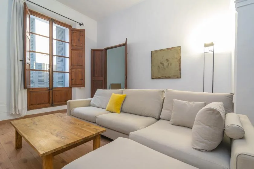 Living room with light-colored seating, a wooden coffee table, and tall windows.
