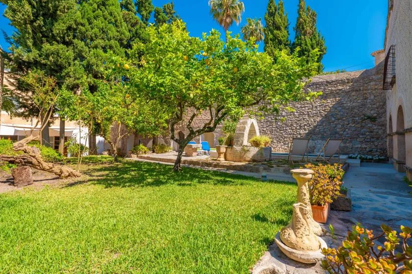 A leafy garden courtyard with a lawn, trees, and stone walls.
