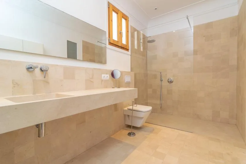 A bright tiled bathroom with a long sink counter and a toilet.