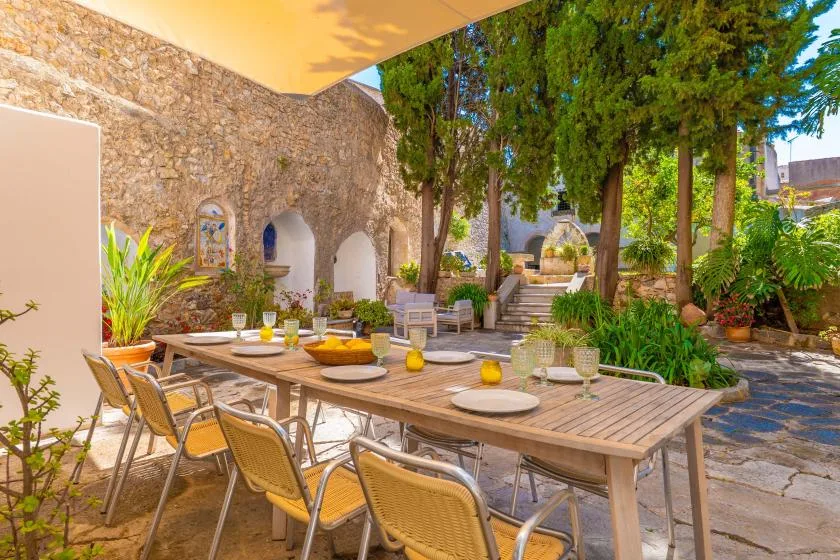 An outdoor dining area with a long table and trees beside a stone wall.