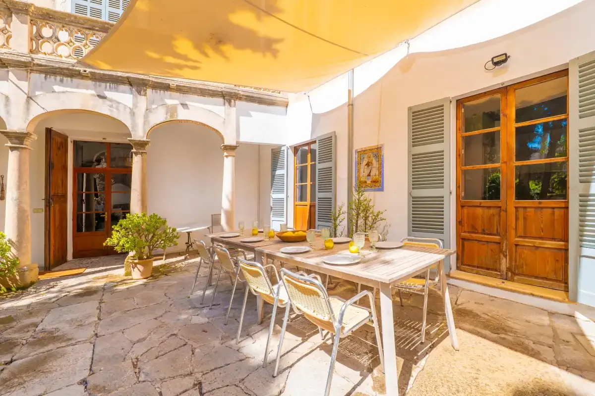 A sunlit courtyard patio has a dining table beneath a yellow canopy.