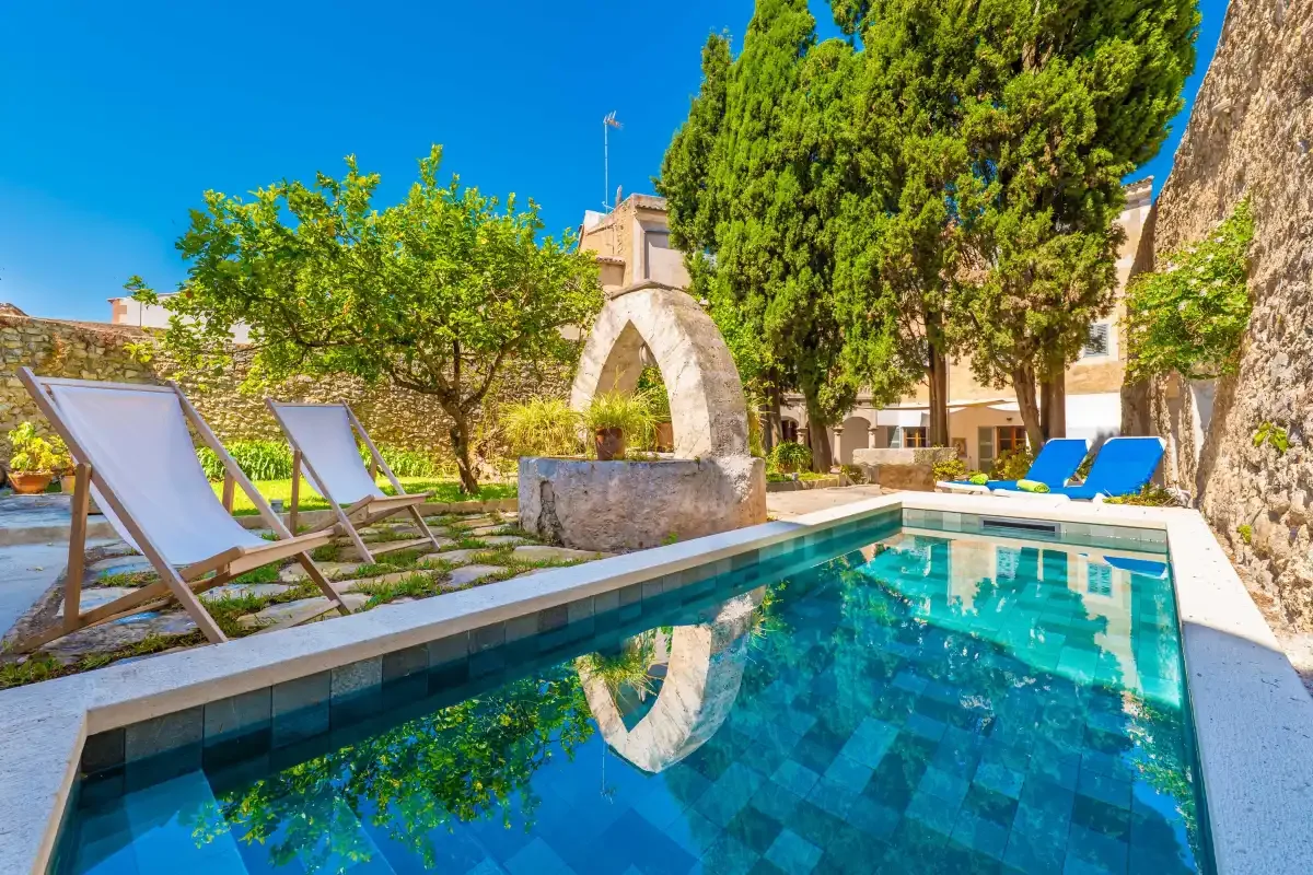 A courtyard pool sits beside a stone fountain and surrounding trees.