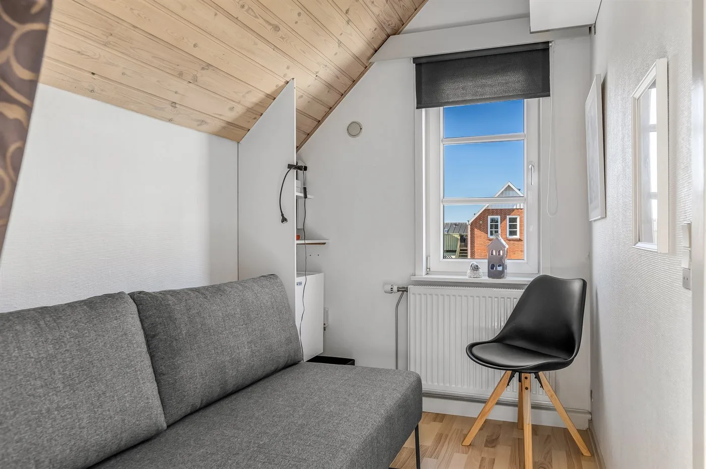 A small sitting area with a gray sofa and a window overlooking a neighboring house.