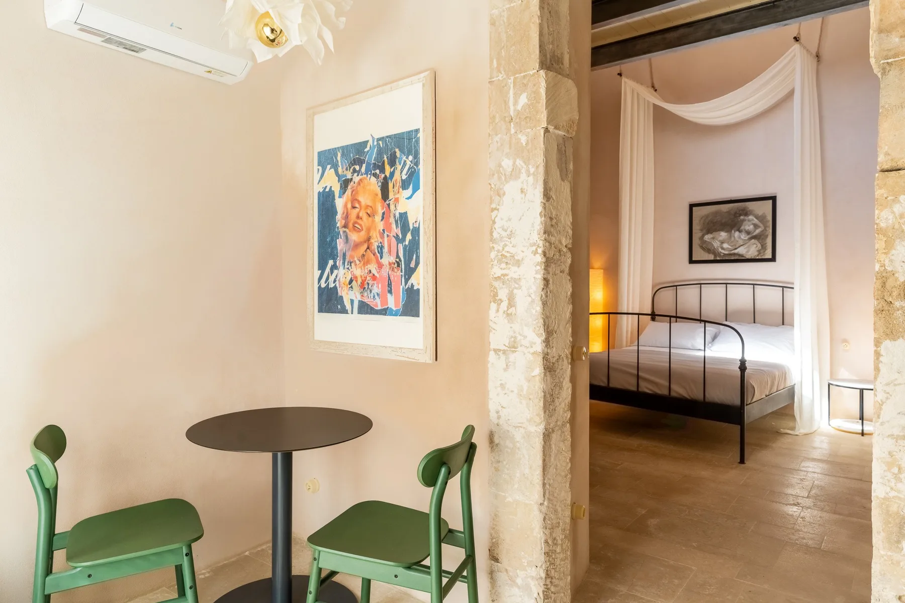 Una pequeña zona de comedor se abre, a través de un arco de piedra, a un dormitorio con cama metálica.