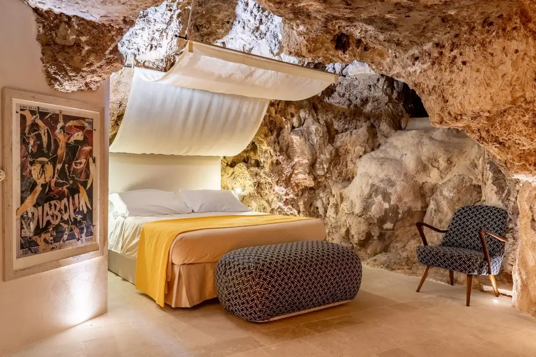 A bedroom with a bed, a patterned bench, and exposed rock walls.
