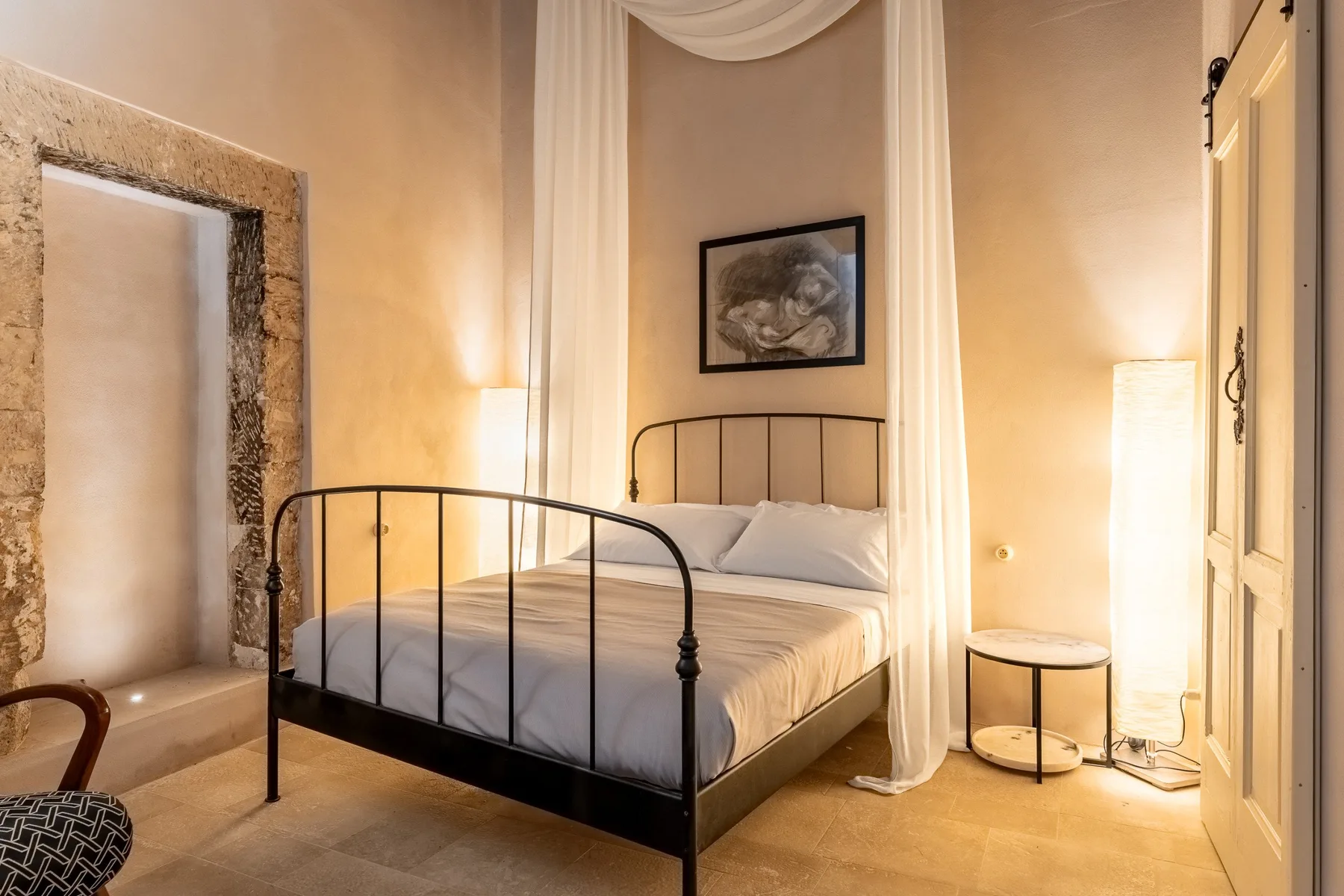 A bedroom with a metal bed, sheer curtains, and a framed picture above the headboard.