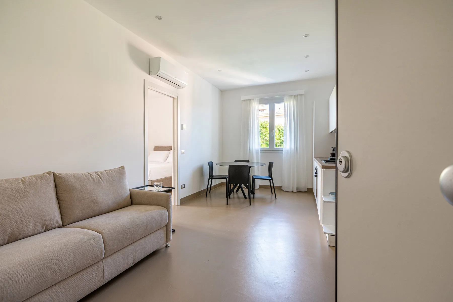 Una luminosa sala de estar tiene un sofá y una pequeña mesa de comedor junto a la ventana.