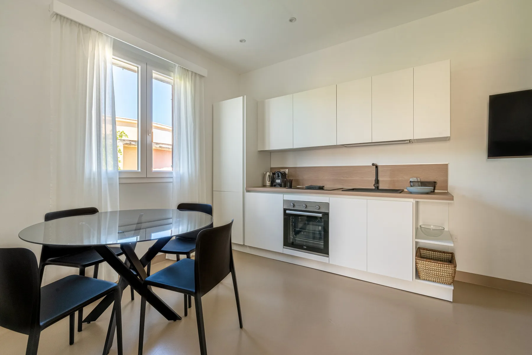 Una cocina luminosa con comedor, gabinetes blancos y una mesa de vidrio.