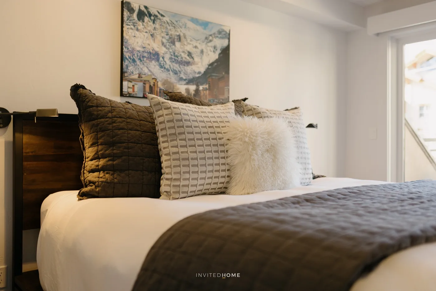 A bedroom with layered pillows and a dark blanket on the bed.