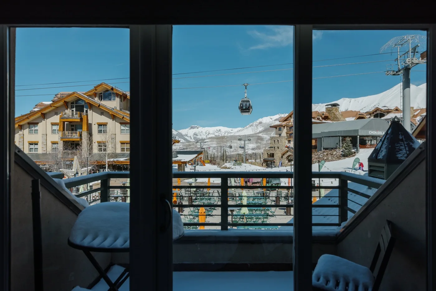 A balcony overlooks a snowy mountain village, with a cable car visible in the distance.