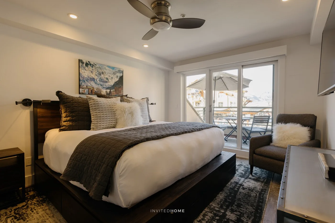 A bedroom with a large bed, an armchair, and glass doors opening to a balcony.