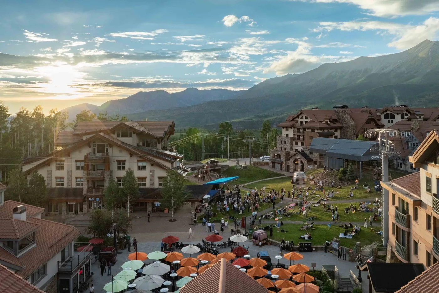 A mountain resort village surrounds a lively outdoor plaza beneath a broad mountain range.