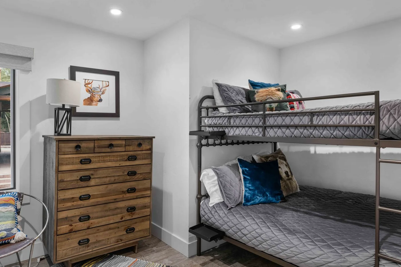 A bedroom with a metal bunk bed, wooden dresser, and framed artwork.
