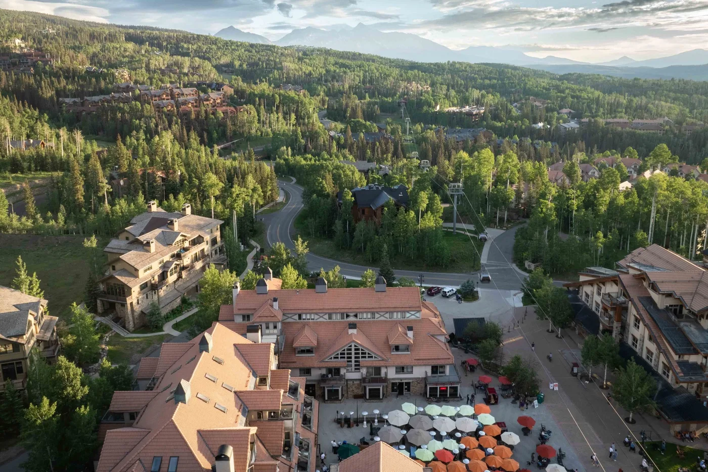 Aerial view of a hillside resort complex surrounded by trees, with outdoor seating below.