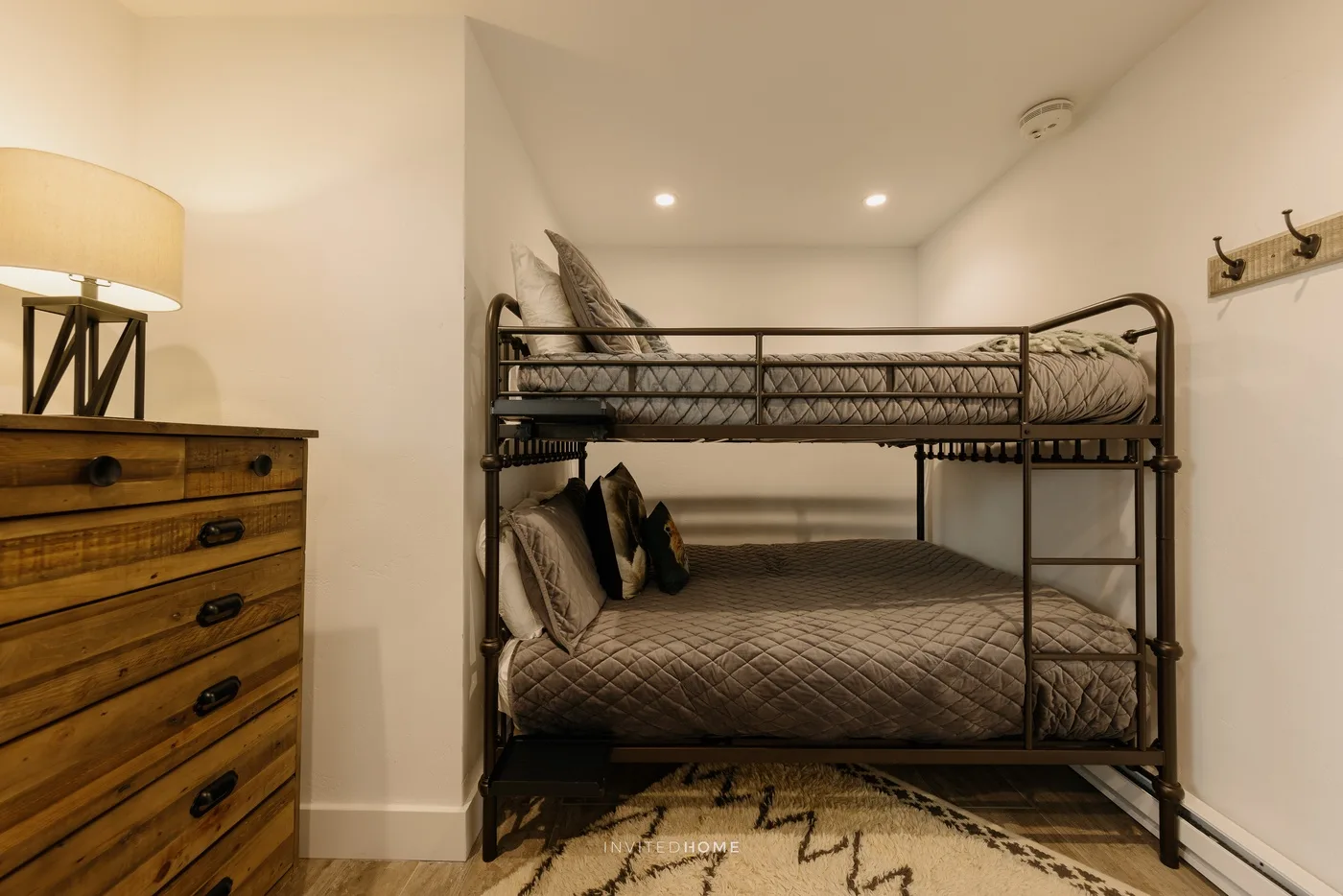 A bedroom with a metal bunk bed and a wooden dresser.