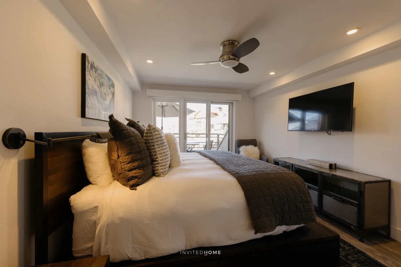 A bedroom with a neatly made bed, wall-mounted television, and glass doors.