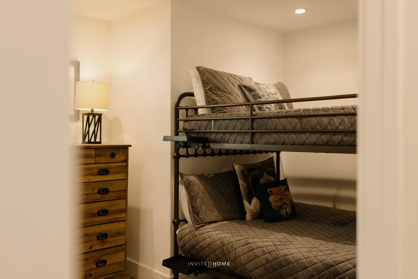 A bunk bed with patterned bedding sits beside a wooden dresser and lamp.