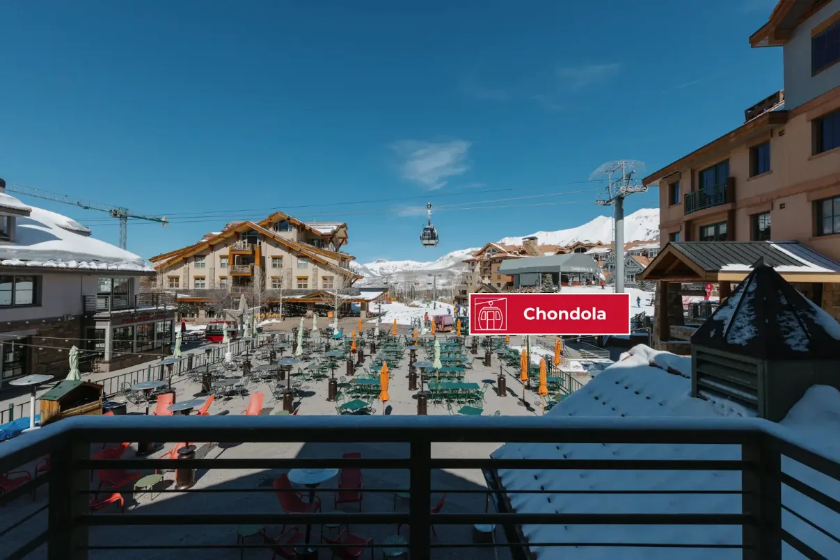 A snowy mountain village with outdoor seating and a gondola lift overhead.