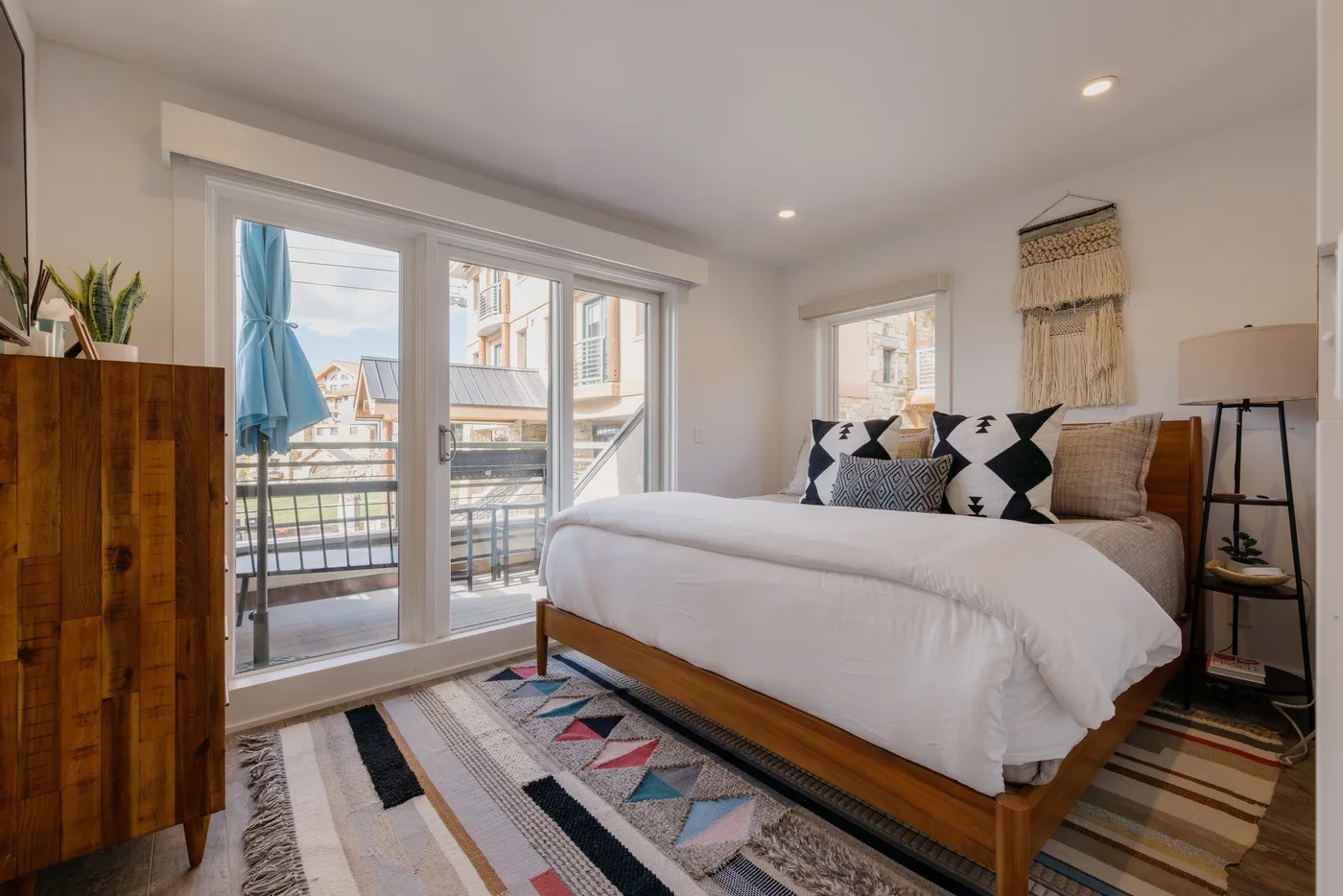 A bright bedroom with a bed beside large glass doors opening onto a balcony.