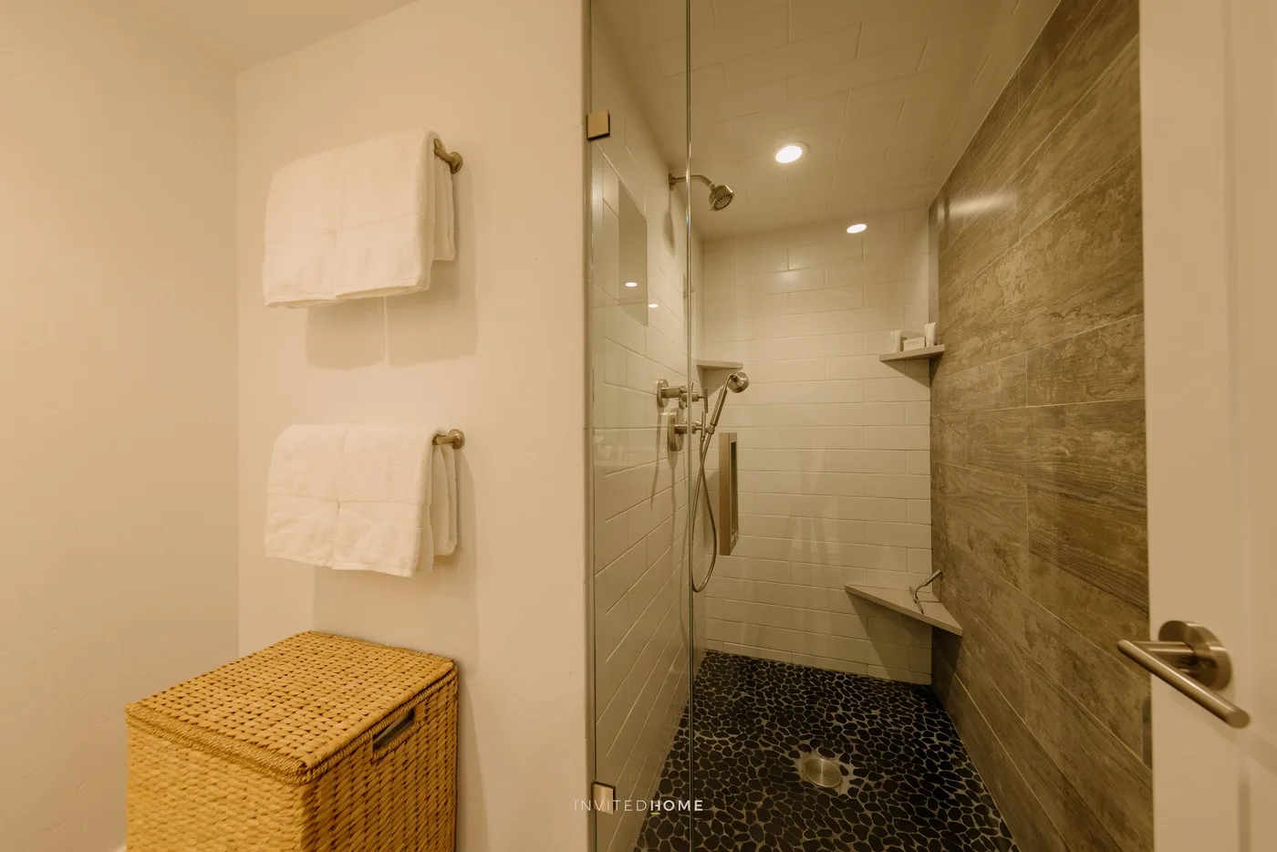 A bathroom with a walk-in shower, dark tiled floor, and towels on the wall.