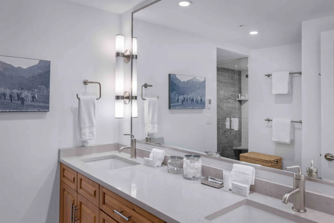A bright bathroom vanity with a wide mirror and a shower in the background.