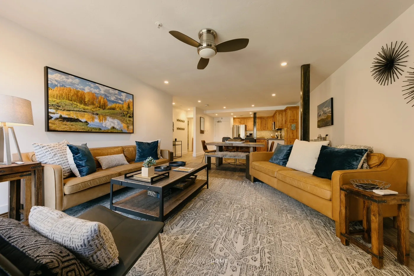 A living room with seating around a coffee table and an open kitchen beyond.