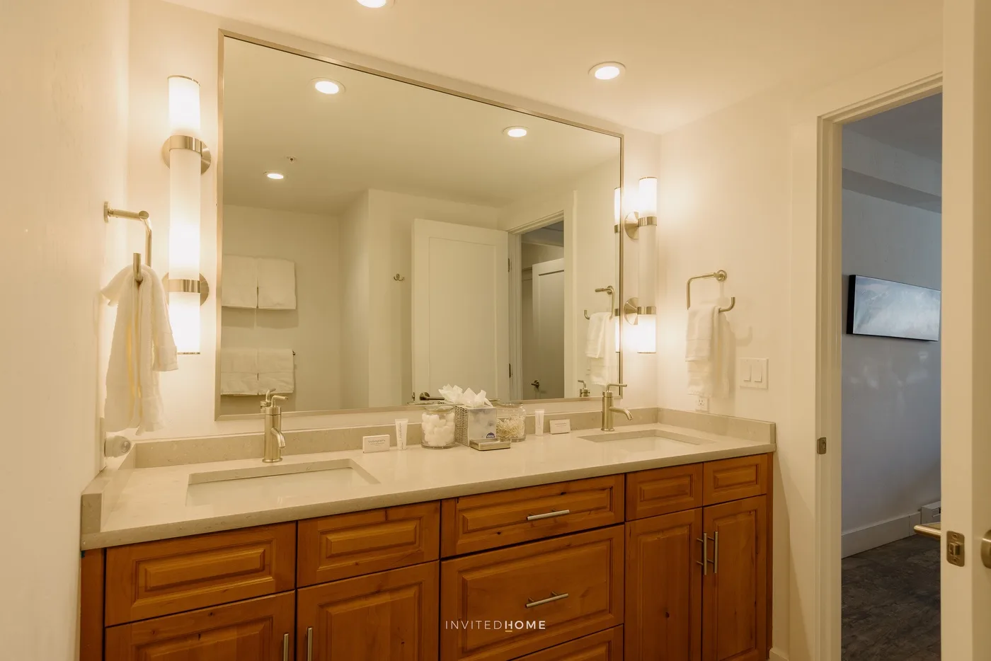 A bright bathroom vanity with a wide mirror and wooden cabinets.