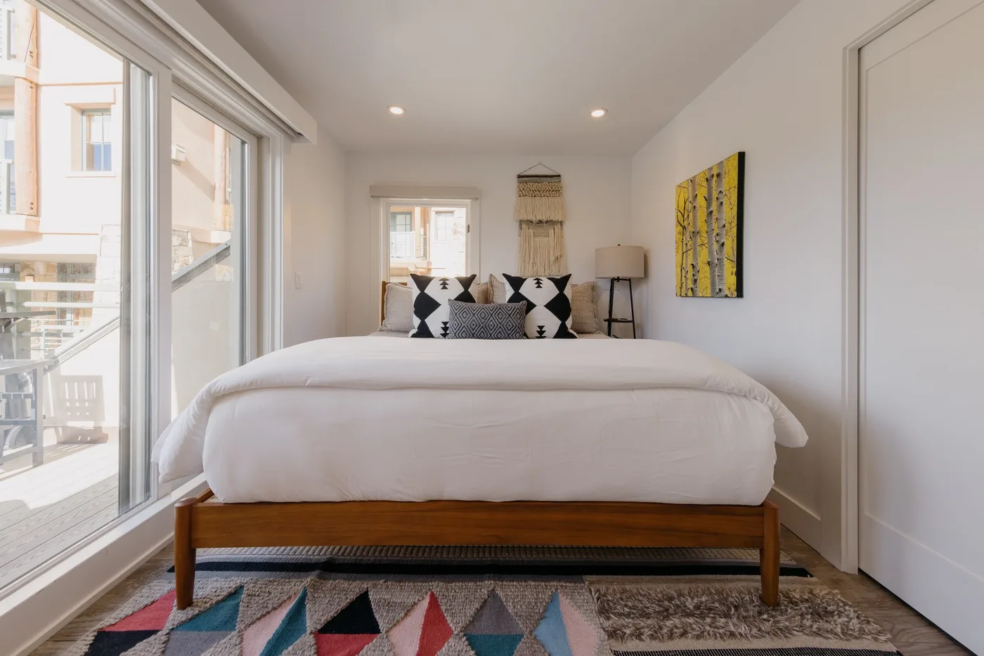 A bright bedroom with a large bed, patterned pillows, and a colorful rug.
