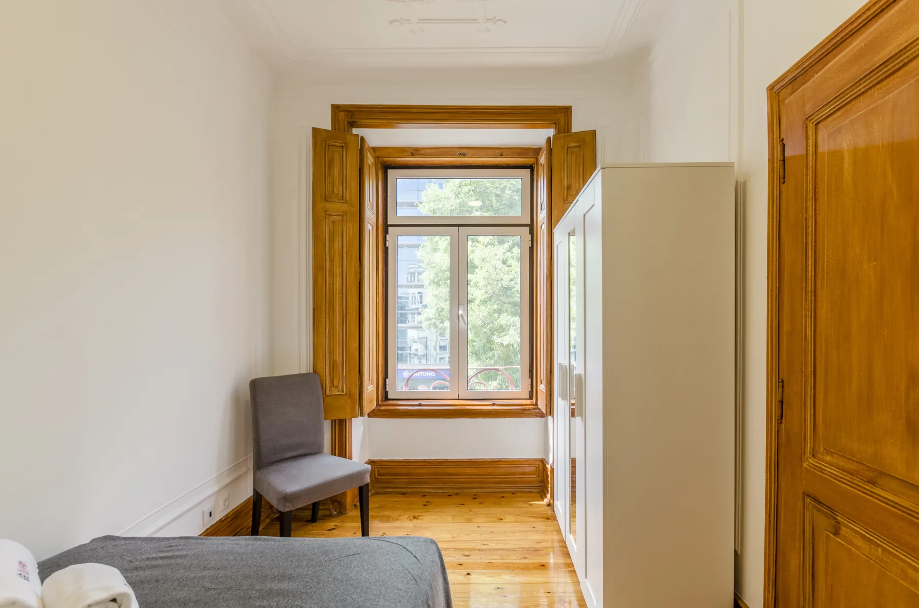 Un dormitorio con una cama, una silla y una ventana con contraventanas de madera.
