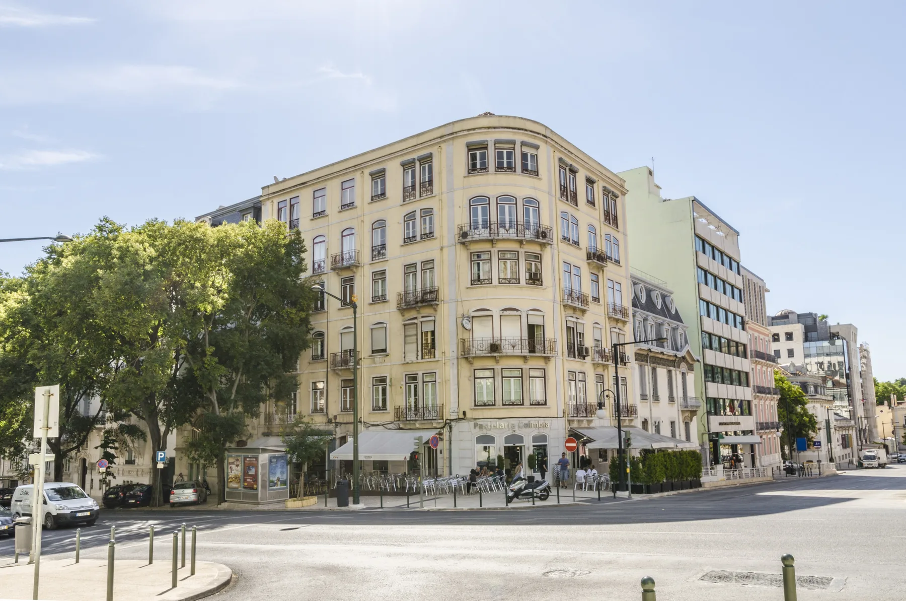 Un edificio de esquina redondeada se alza junto a una calle arbolada.