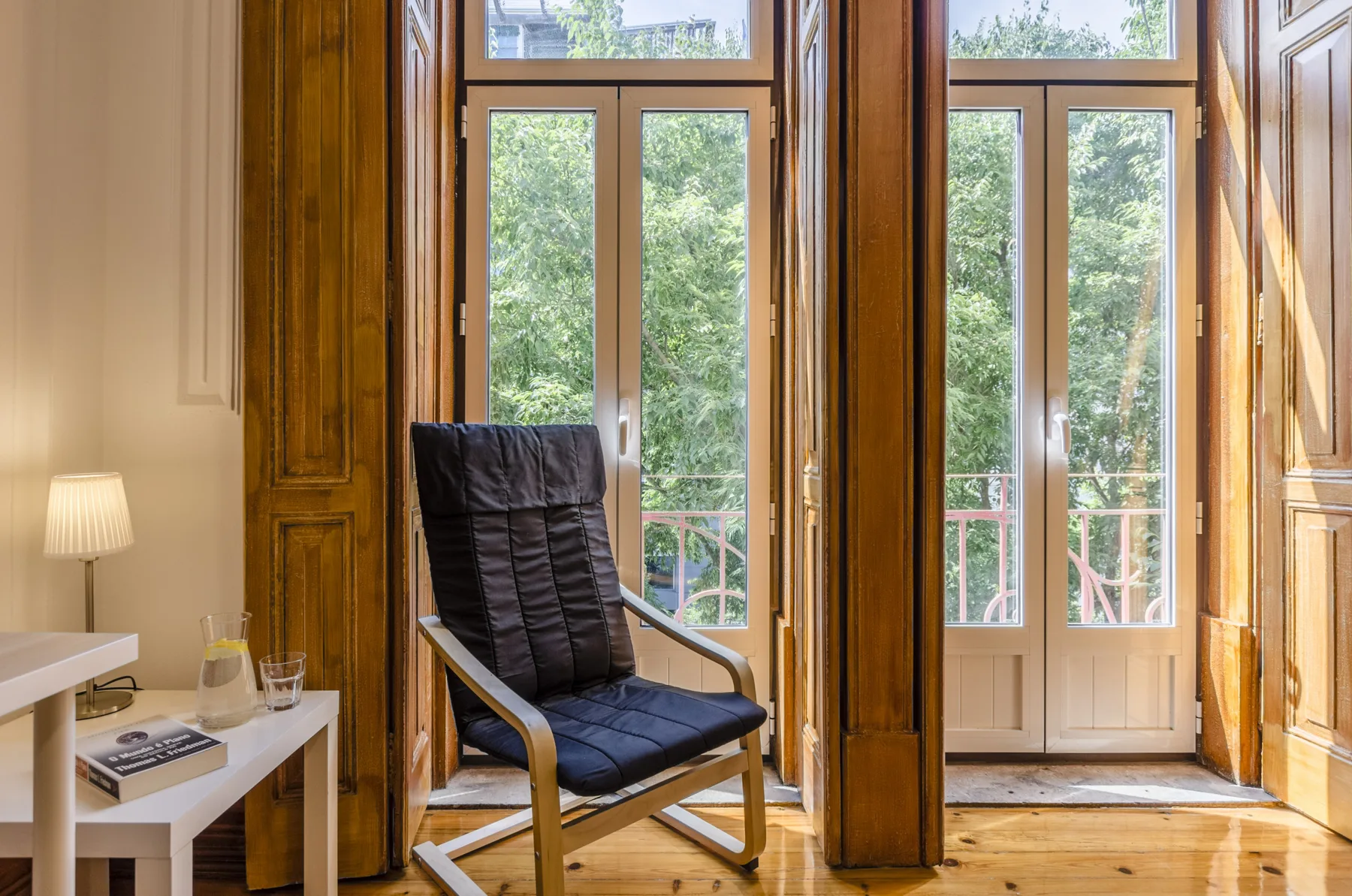 Una zona de estar luminosa con un sillón acolchado junto a ventanas altas.