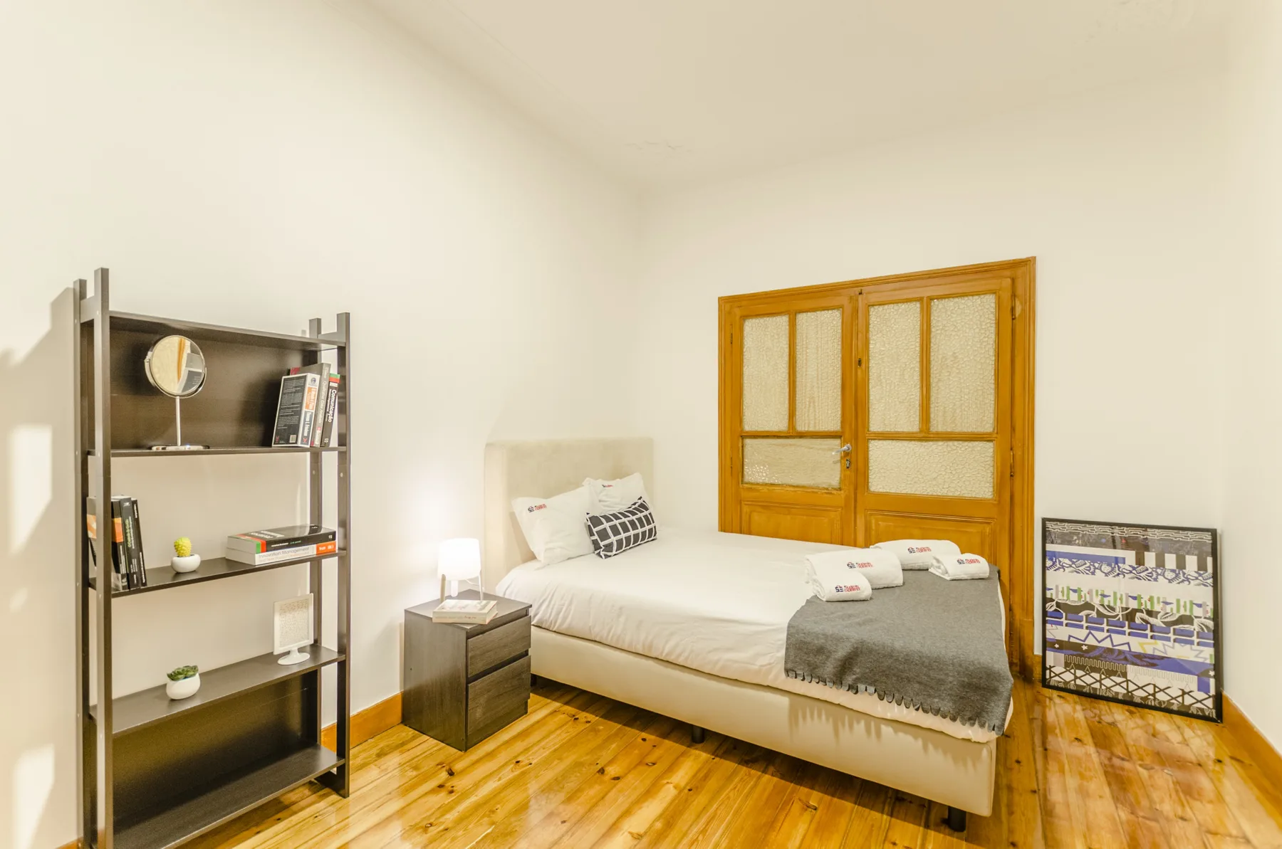 Un dormitorio con cama, estantería y suelo de madera.