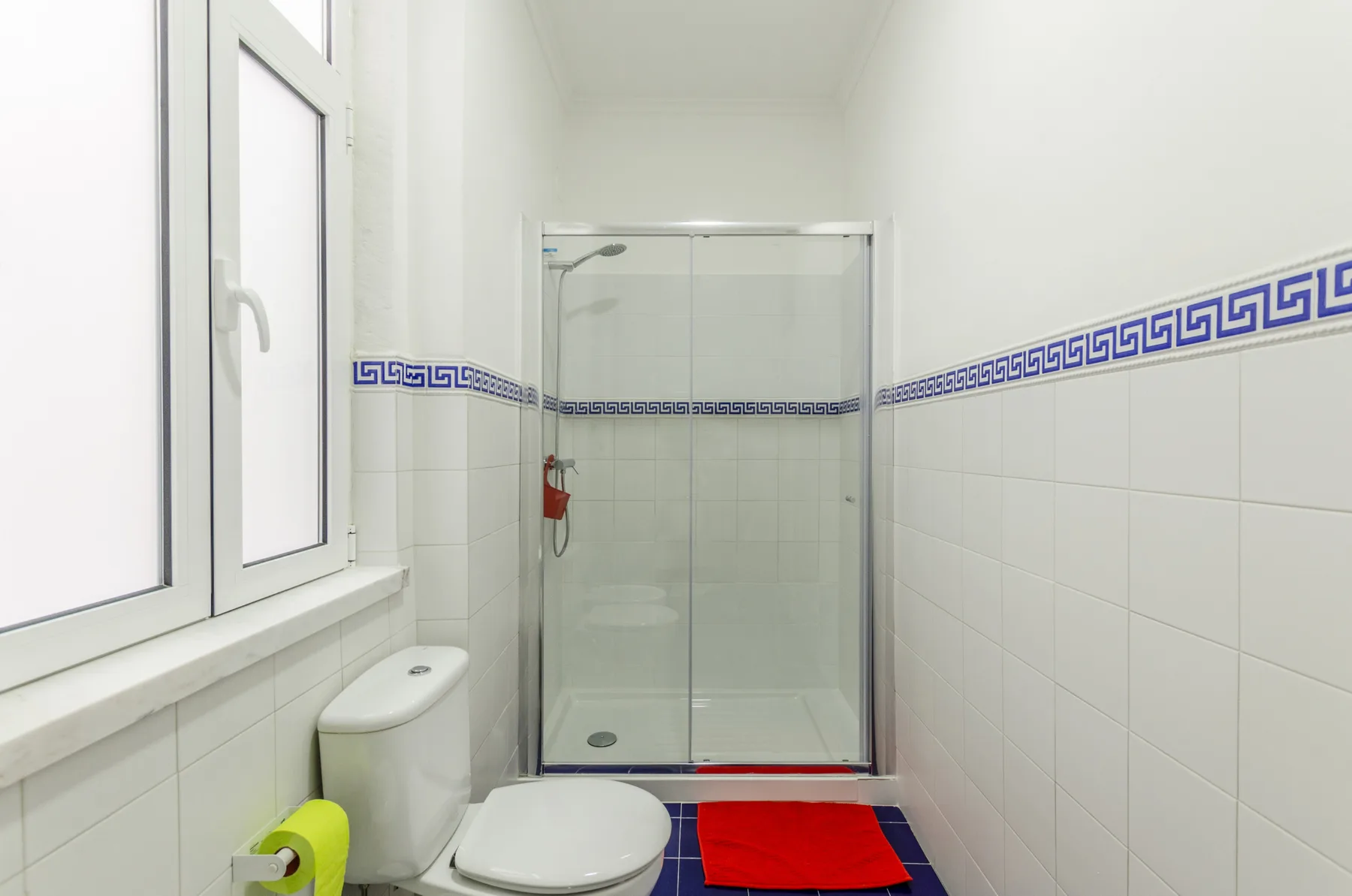 Un baño alicatado con una ducha de vidrio y una ventana.