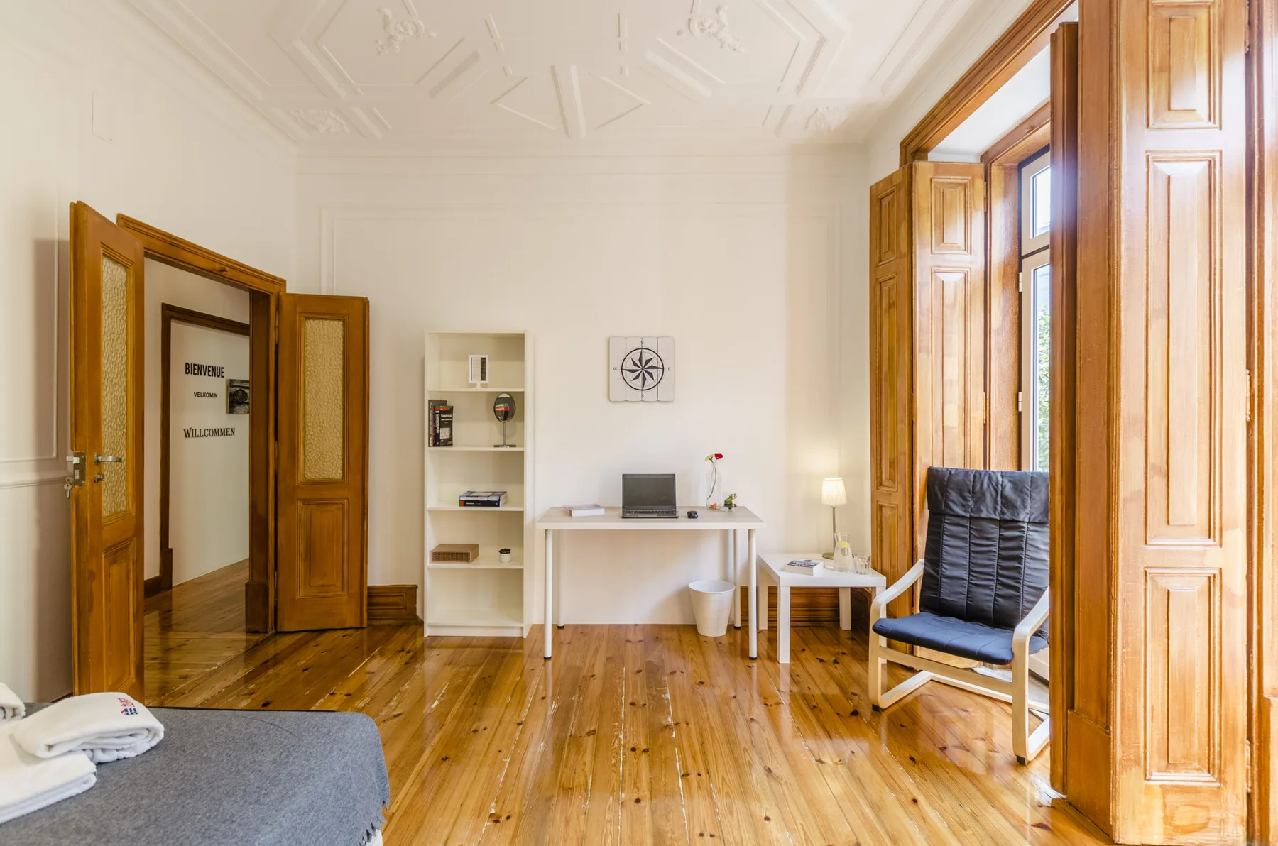 Una habitación luminosa con escritorio, estantería y una silla junto a ventanas altas.