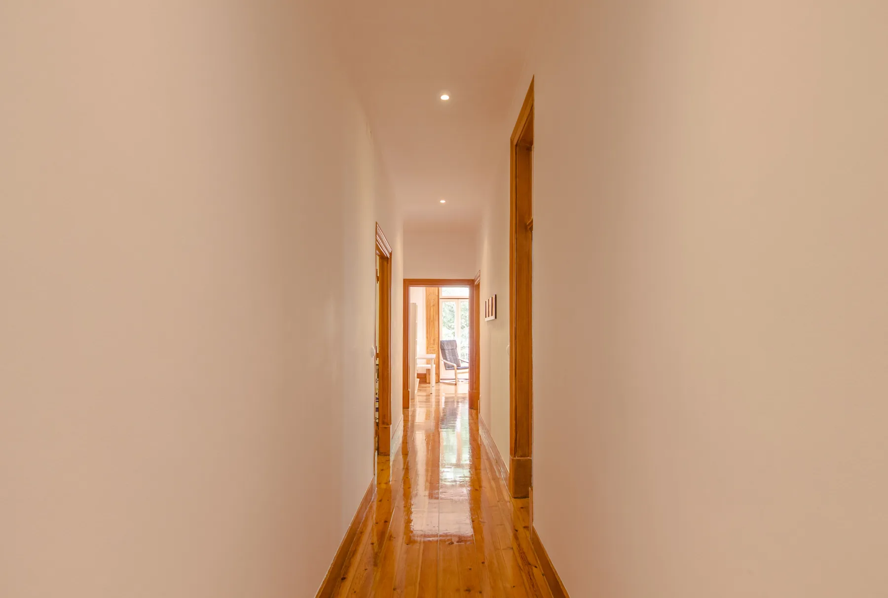 Un pasillo estrecho con suelo de madera y puertas abiertas.