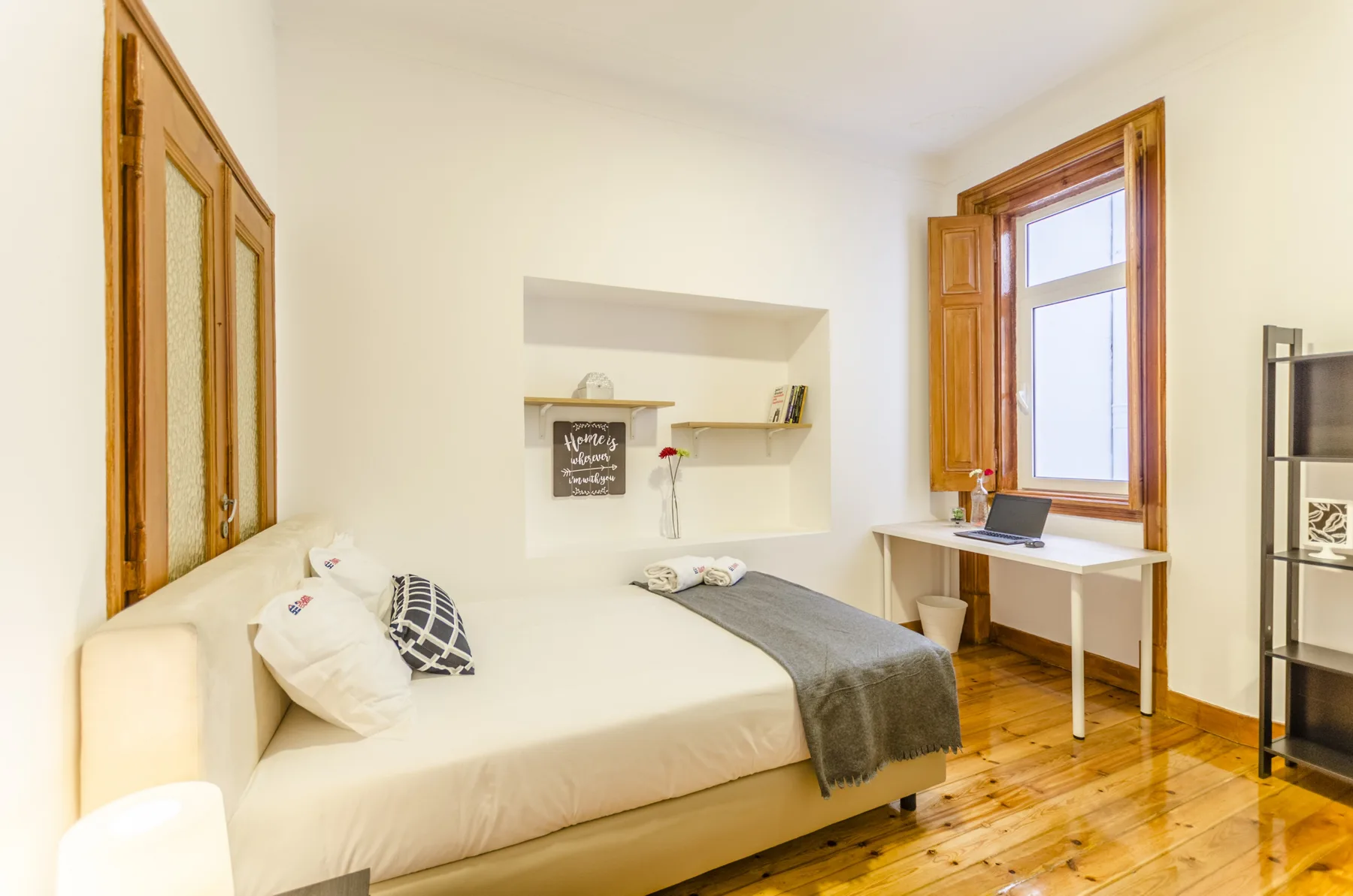 Un dormitorio con una cama, un escritorio bajo la ventana y suelo de madera.