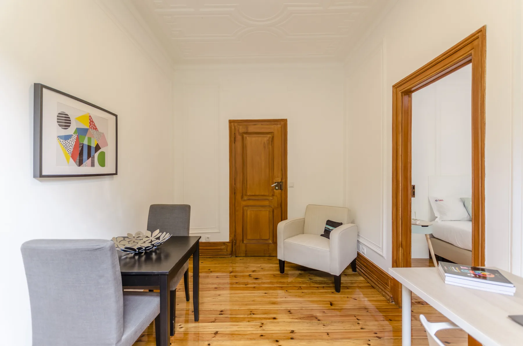 Una luminosa zona de estar con mesa, sillón y puertas de madera.