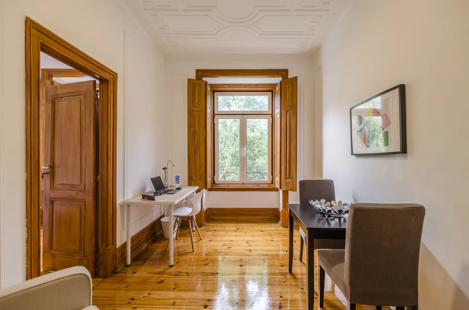Una habitación luminosa con escritorio, mesa de comedor y una ventana grande.