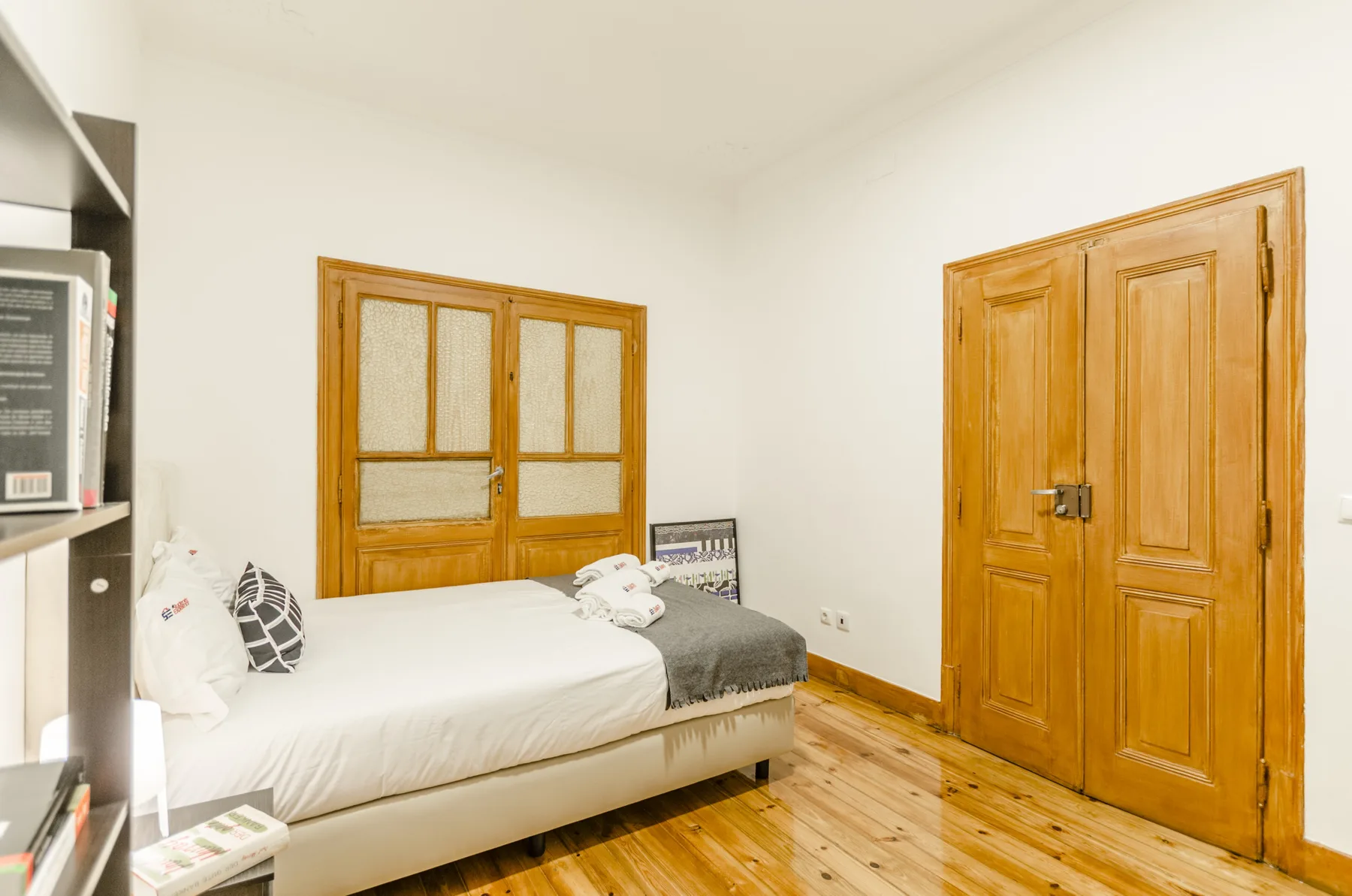 Un dormitorio con una cama junto a ventanas de madera y una puerta de paneles.