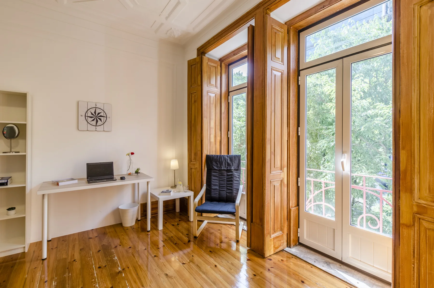 Una habitación luminosa con escritorio, asiento y ventanas altas que dan a un balcón.
