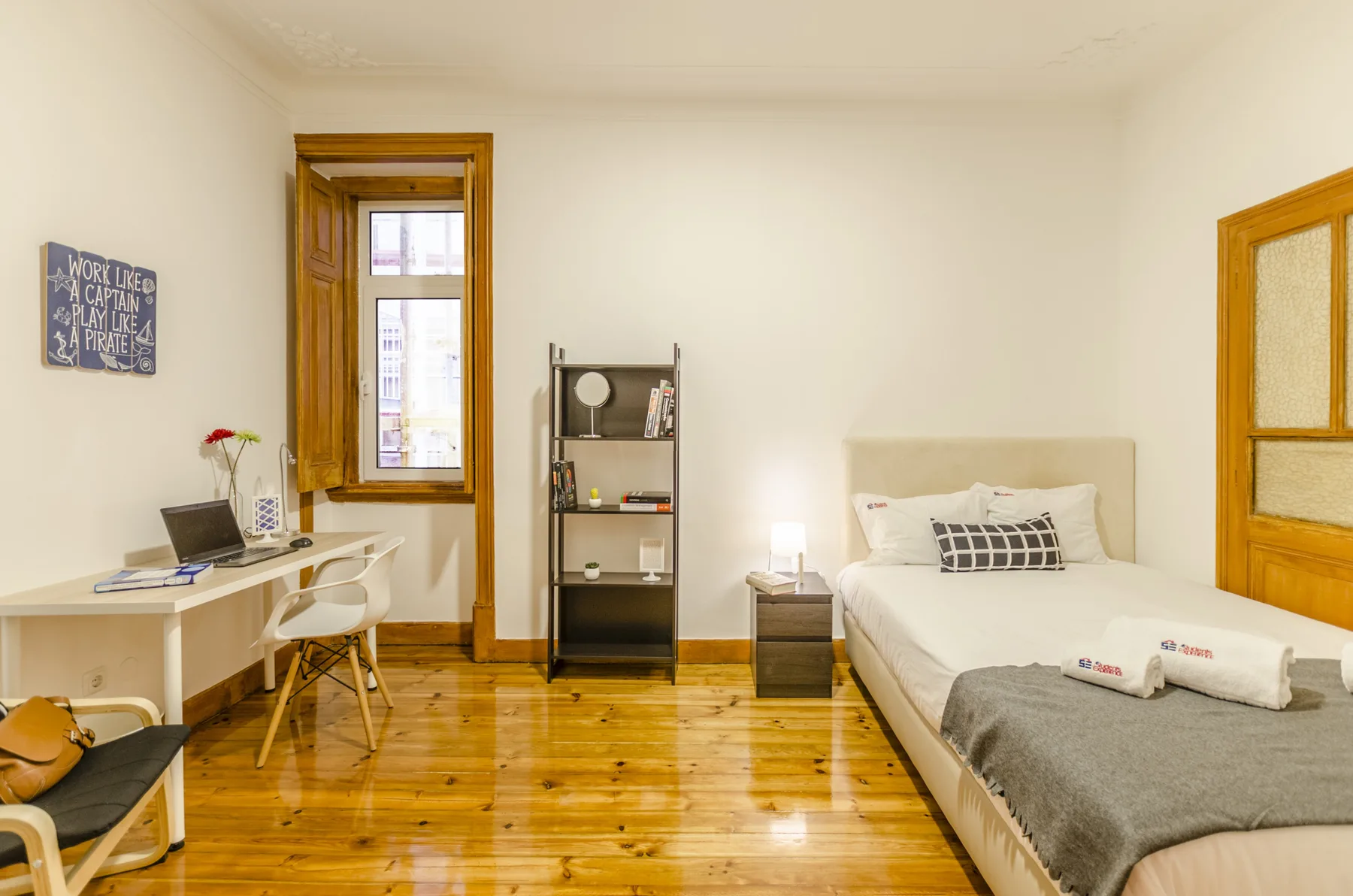 Dormitorio con una cama bien arreglada, un escritorio y suelo de madera.