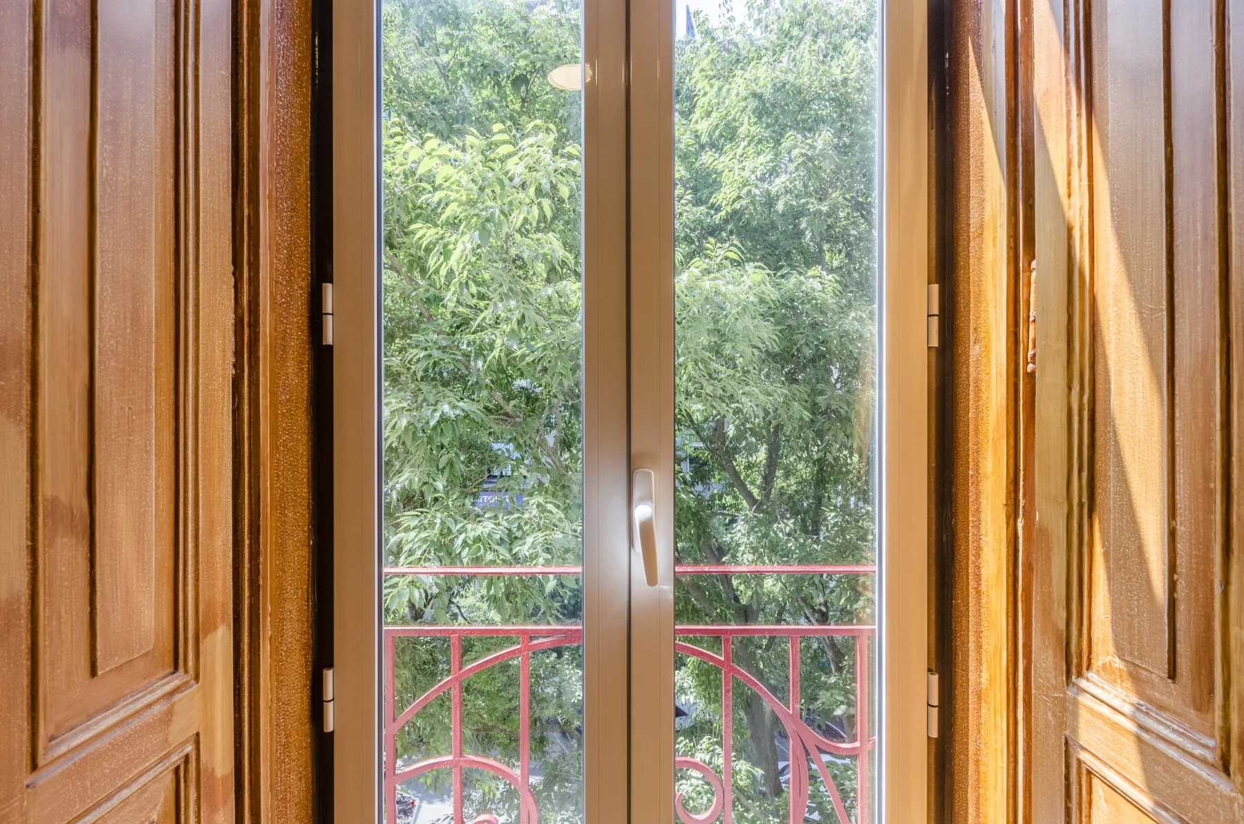 Una puerta de vidrio con marco de madera da a árboles frondosos y una barandilla roja.
